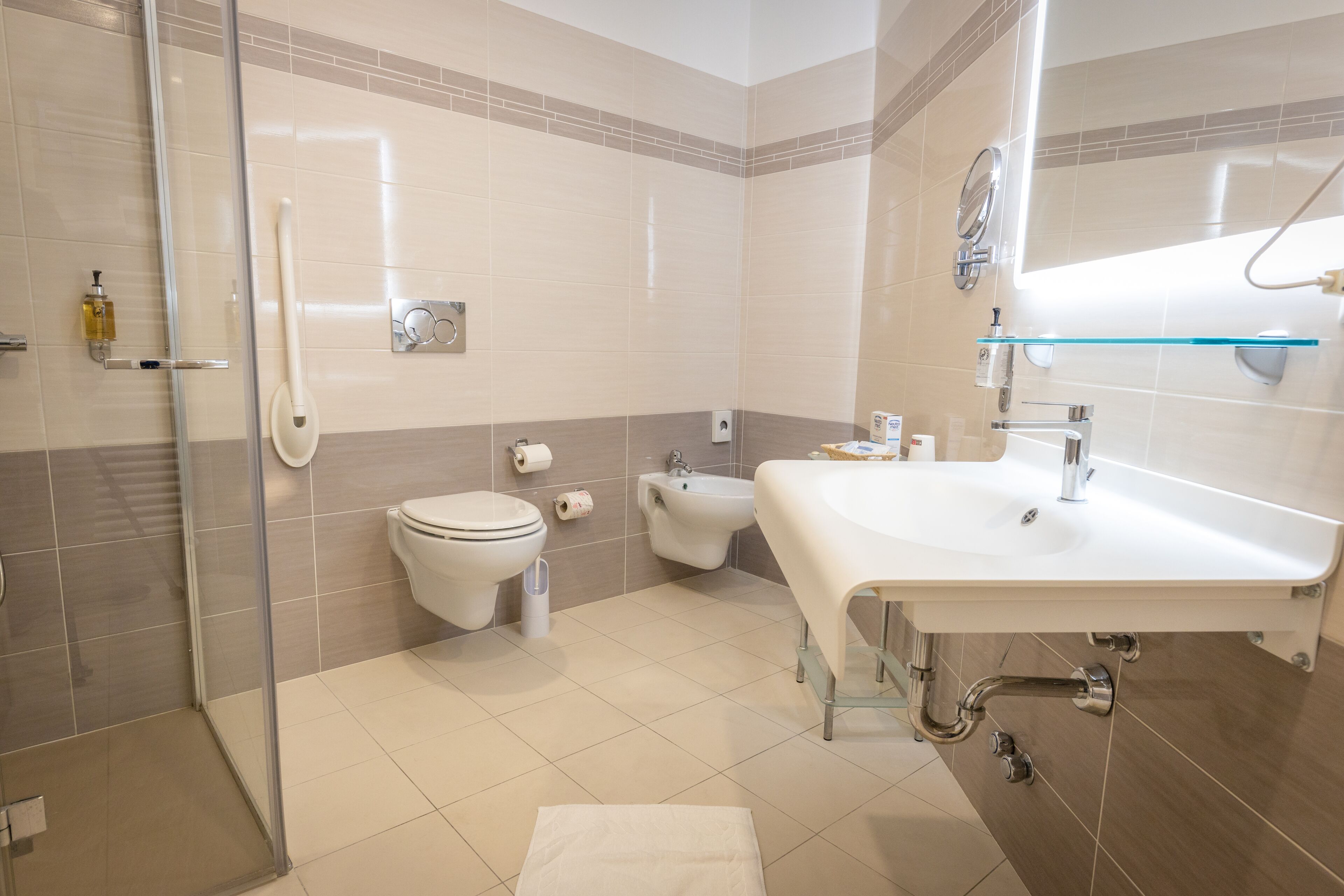A modern bathroom with a glass shower enclosure, a toilet, bidet, and a large sink with a mirror.