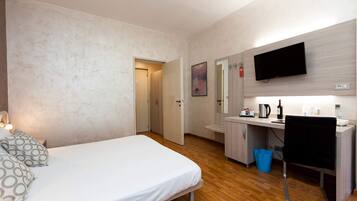 Habitación de hotel con cama, escritorio con computadora, televisor y una pequeña cocina.