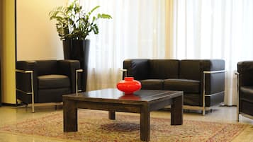 Una sala moderna con una mesa de centro marrón oscuro, dos sofás de cuero negro y una planta grande en maceta.