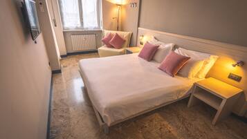 A hotel room with a large bed, bedside tables, a lamp, a TV, and a window with curtains.
