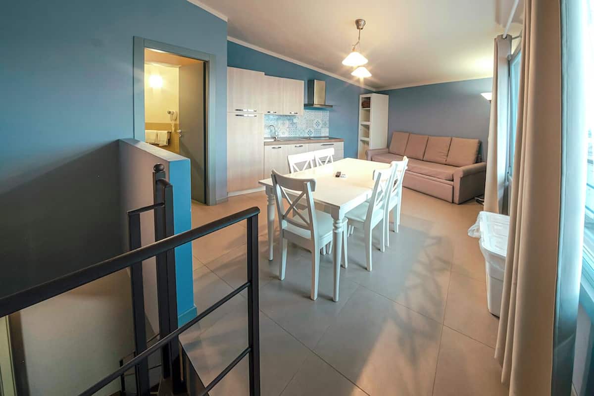 A modern kitchen with white cabinets, a dining table with chairs, and a sofa in a living area.