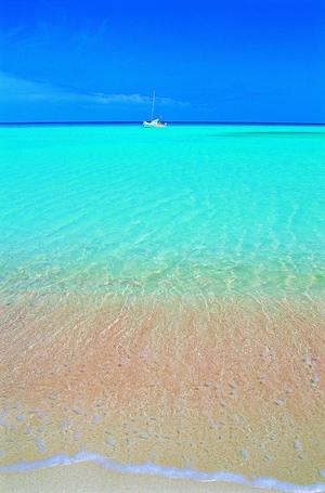A beach with clear turquoise water and a boat in the distance.
