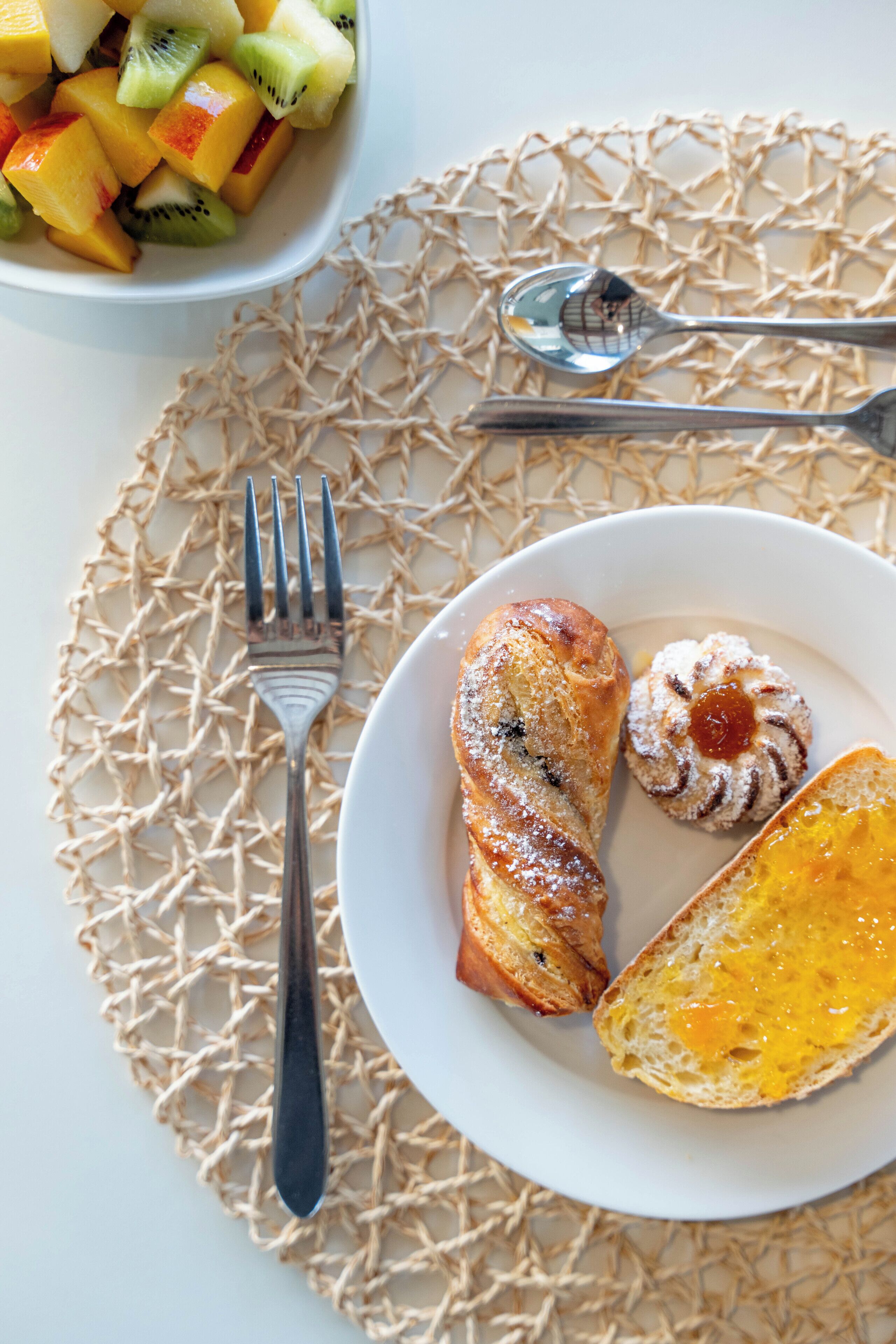 A plate with croissant, a pastry, and a piece of bread with cheese on a white plate.