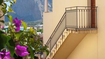 A building with a staircase leading to a balcony, a mountain in the background, and purple flowers in the foreground.