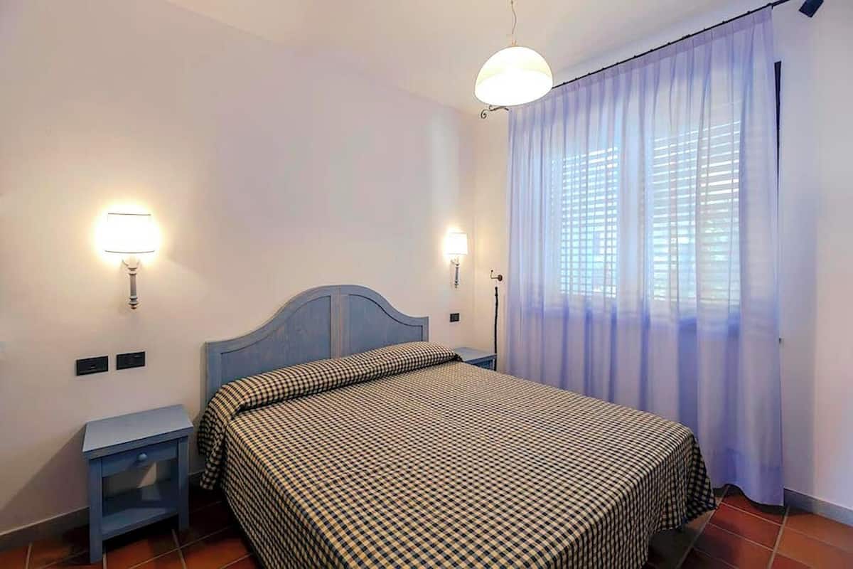 A bedroom with a bed, two bedside tables, a nightstand, a lamp, and a window with curtains.