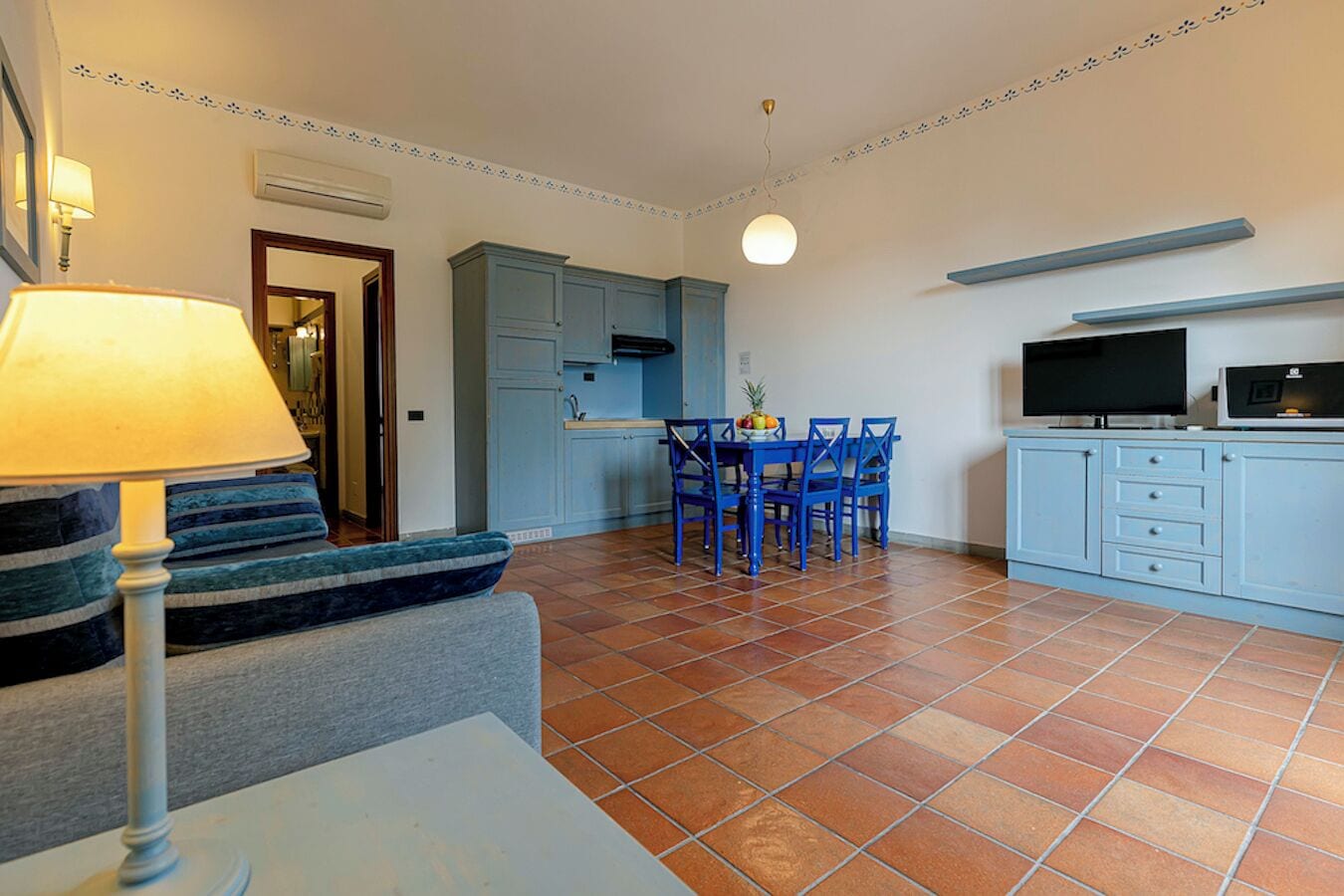 Un espacio habitable compacto con sofá, una mesa de comedor con sillas, televisor y una cocina con armarios y una lámpara colgante.