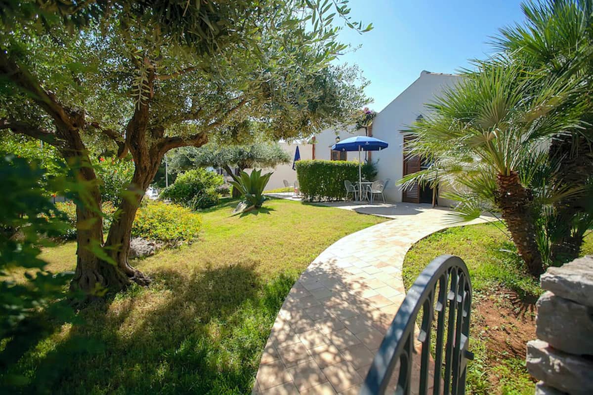 A pathway leading to a building with outdoor seating and a blue umbrella.