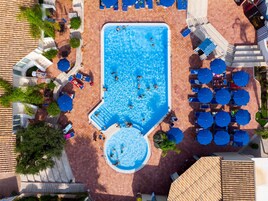 Vista aérea de un área de piscina con múltiples sillas de descanso y sombrillas.