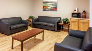 Una sala de estar con dos sofás de cuero negro, una mesa de centro de madera y una mesita auxiliar con una planta. Hay un microondas y una tetera sobre un mueble de madera.