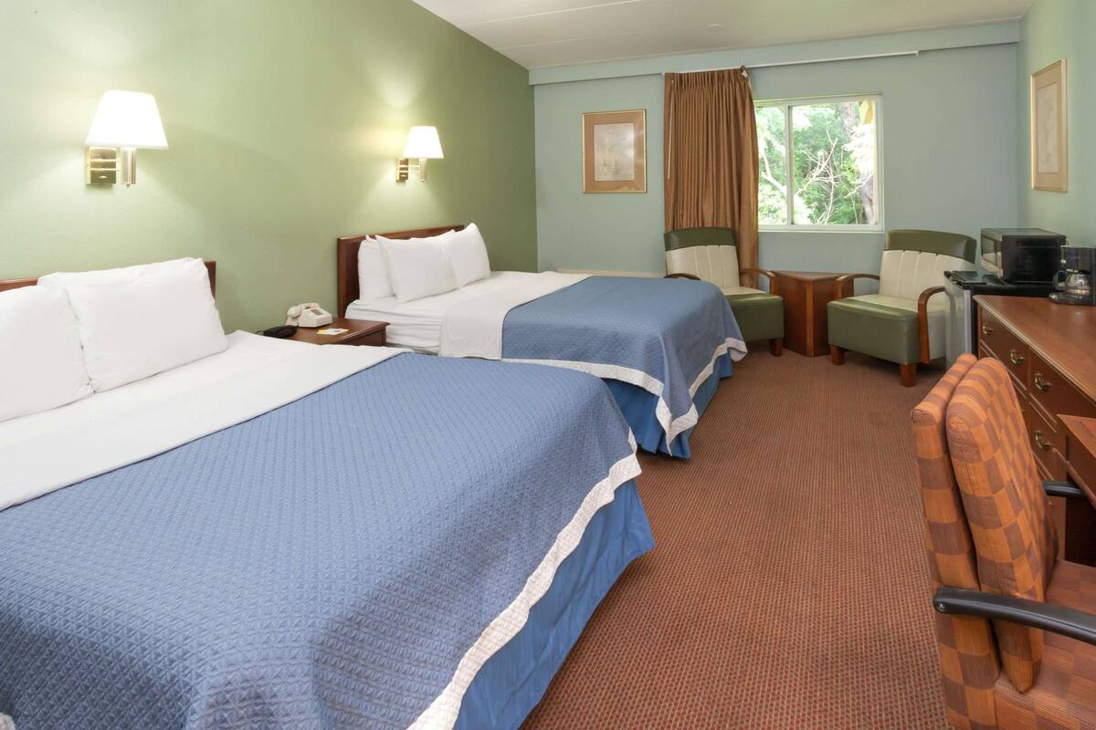 A hotel room with two beds, a desk, a chair, and a window with curtains.