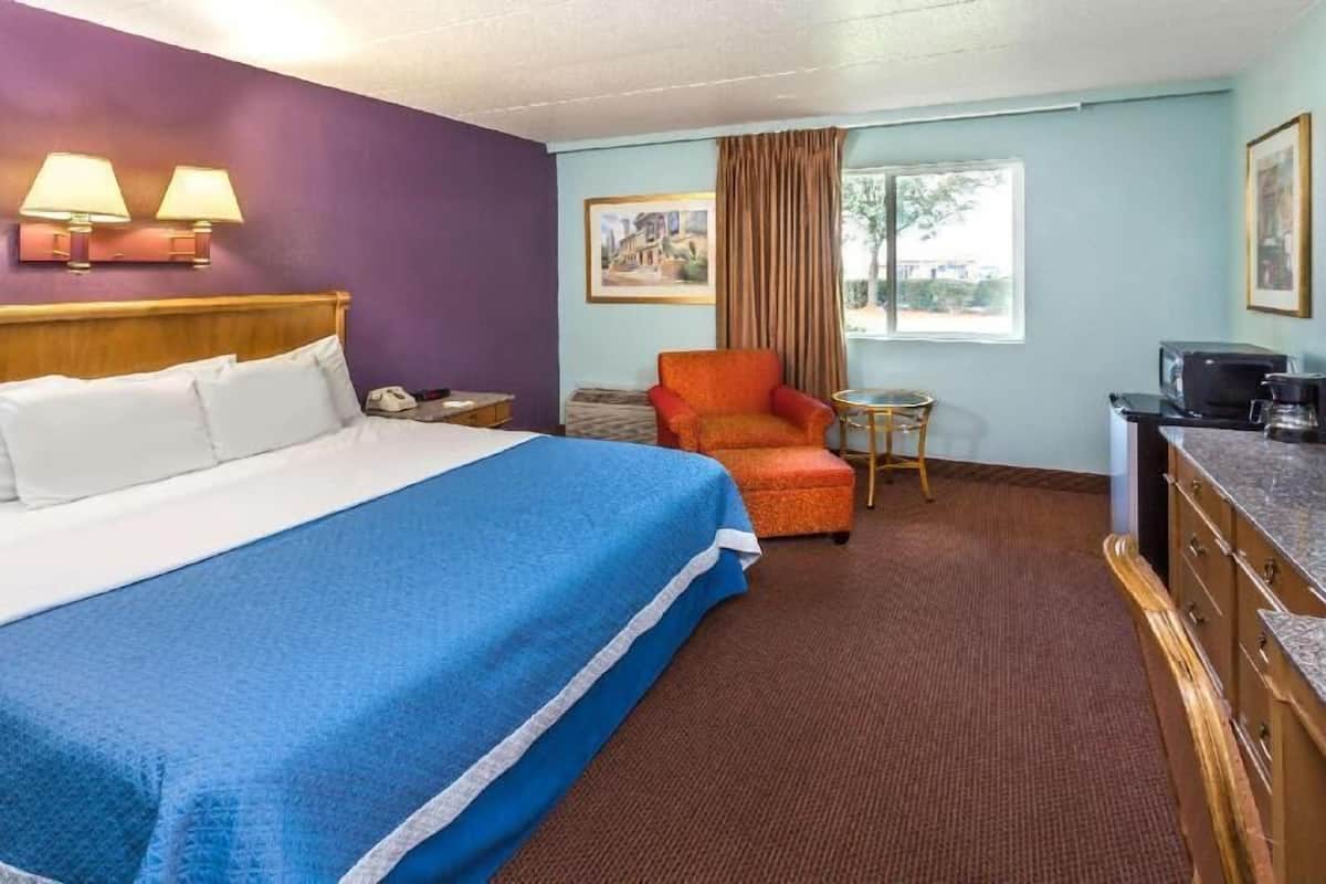 A hotel room with a bed, a chair, a desk, a television, and a window with curtains.