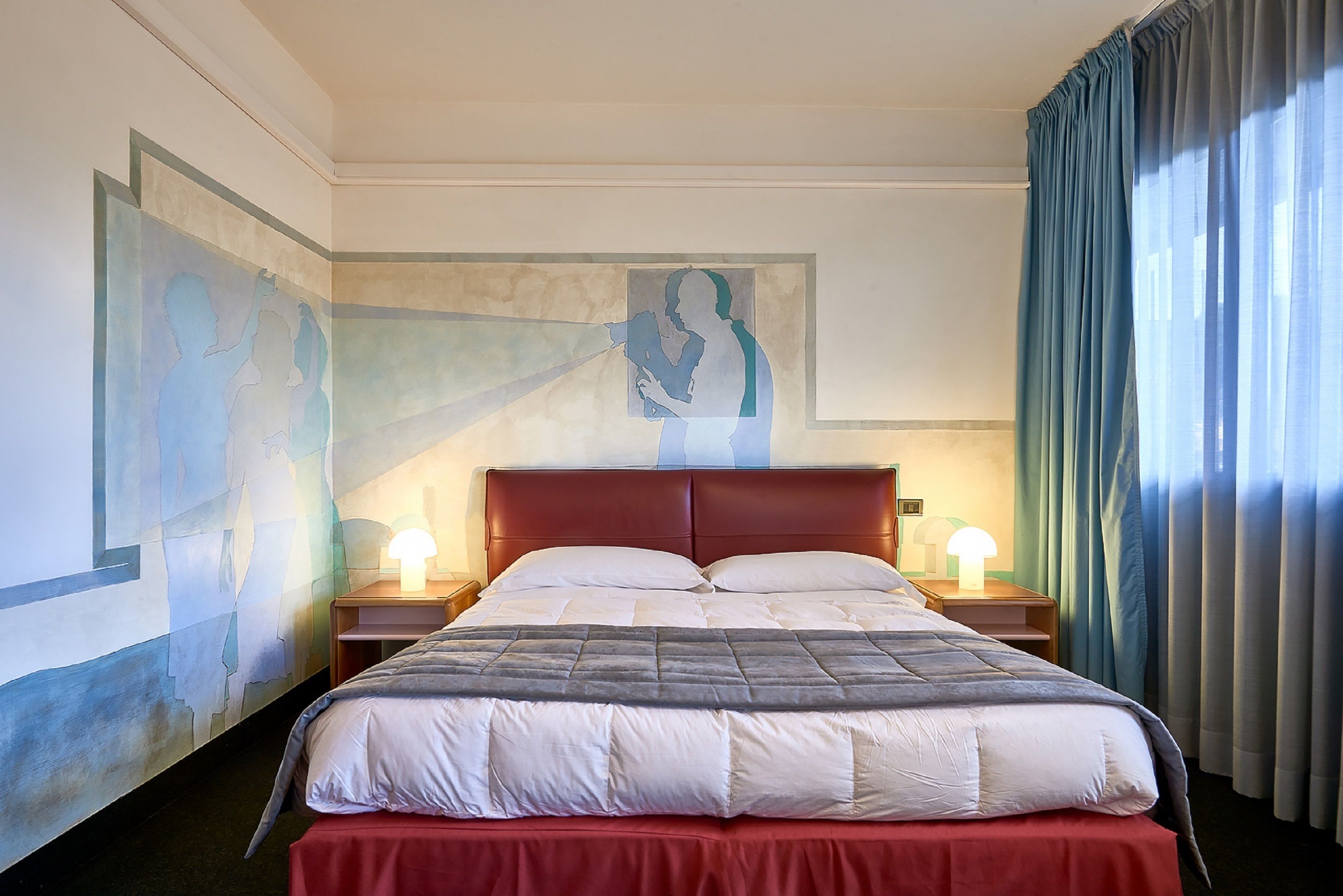 A hotel room with a large bed, two bedside tables with lamps, a headboard, and artwork on the walls.