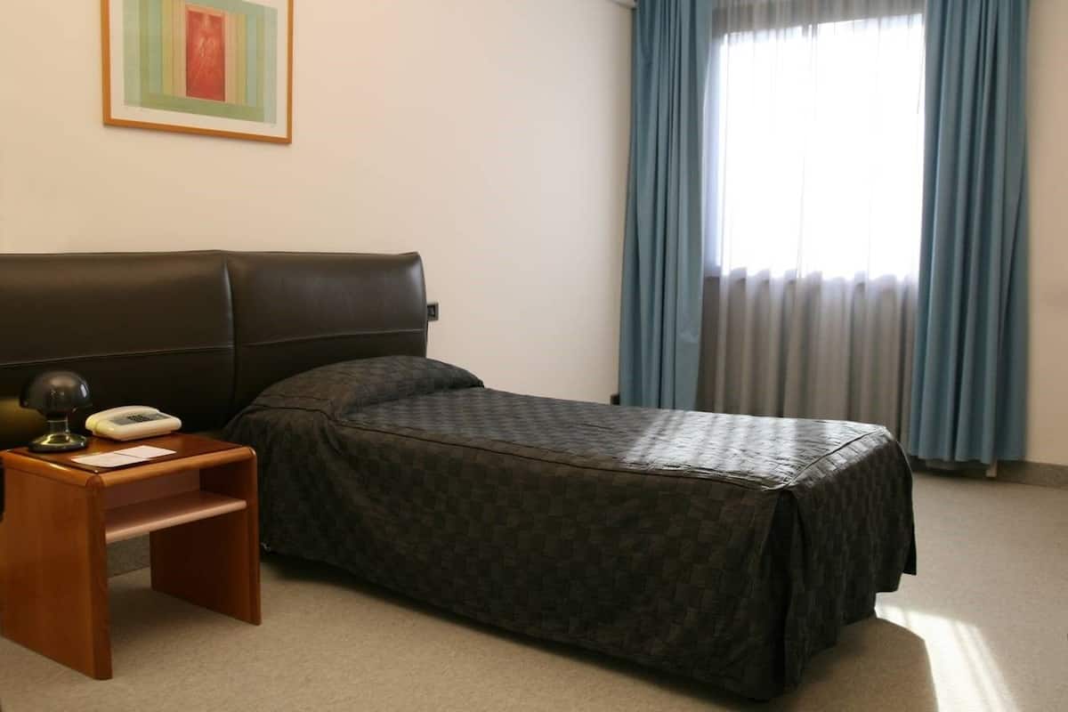 A hotel room with a single bed, a nightstand with a lamp, a telephone, and a framed picture on the wall.