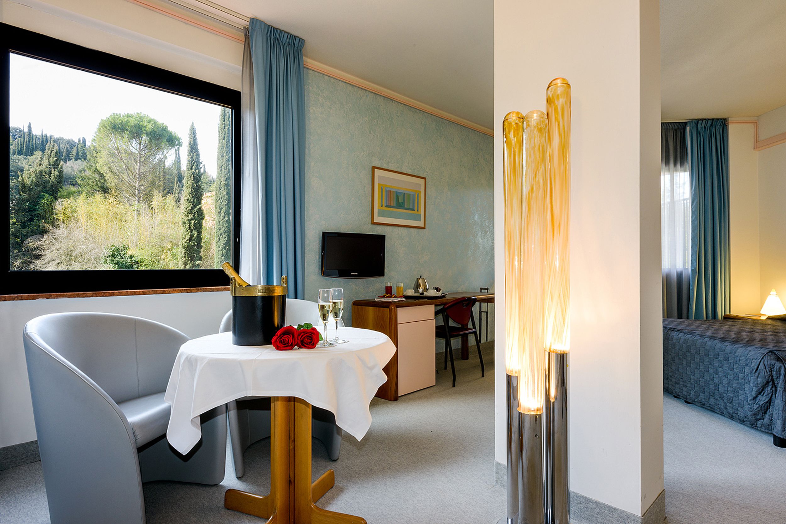 Een hotelkamer met een eethoek, bureau, televisie en bed.