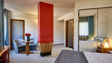 Una habitación de hotel con una cama, un escritorio con silla, una mesita con un florero y un espejo grande.