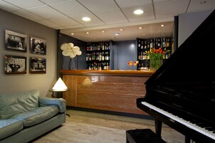 Un vestíbulo con un piano de cola, una zona de bar con varios botelleros y un sofá.