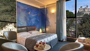 Habitación de hotel con una cama grande, vistas a un castillo y un balcón con mesa y sillas.