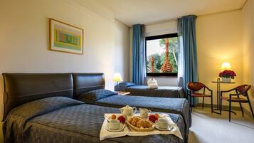 Camera d'albergo con due letti, un'area pranzo con tavolo e sedie, e una finestra con tende.