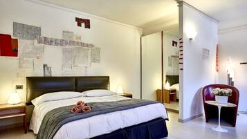 A hotel room with a large bed, a bedside table with a lamp, a chair with a flower pot, and a mirror on the wall.