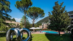 Zona de piscina con cielo despejado, árboles y un edificio al fondo.