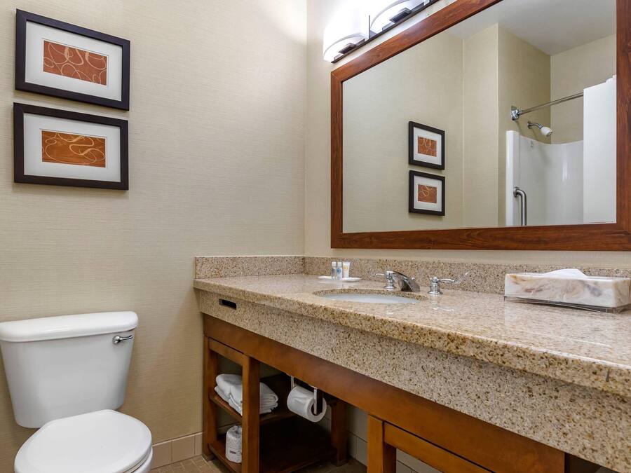 A bathroom with a toilet, sink, and mirror. There are framed pictures on the wall.