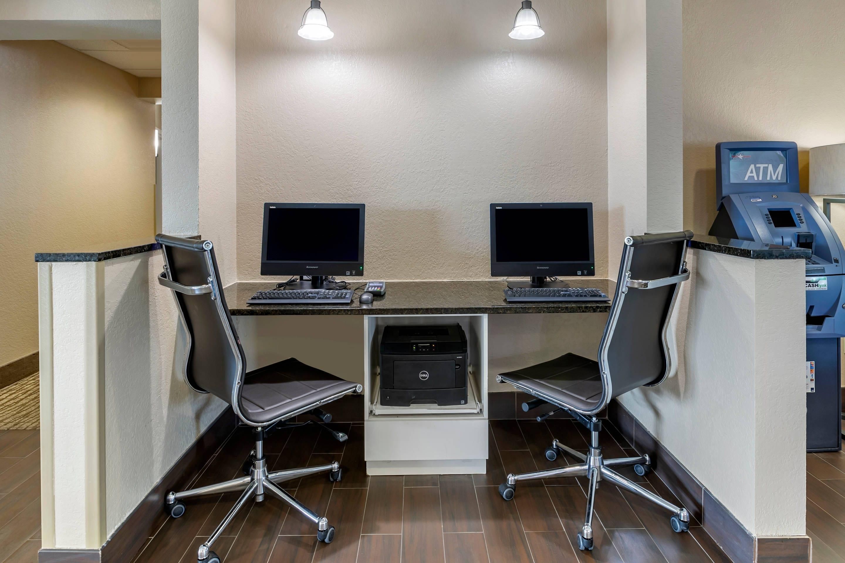 Un espace de travail comprenant deux bureaux, deux chaises, une imprimante et un distributeur automatique de billets.