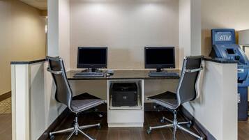 Un espace de travail comprenant deux bureaux, deux chaises, une imprimante et un distributeur automatique de billets.