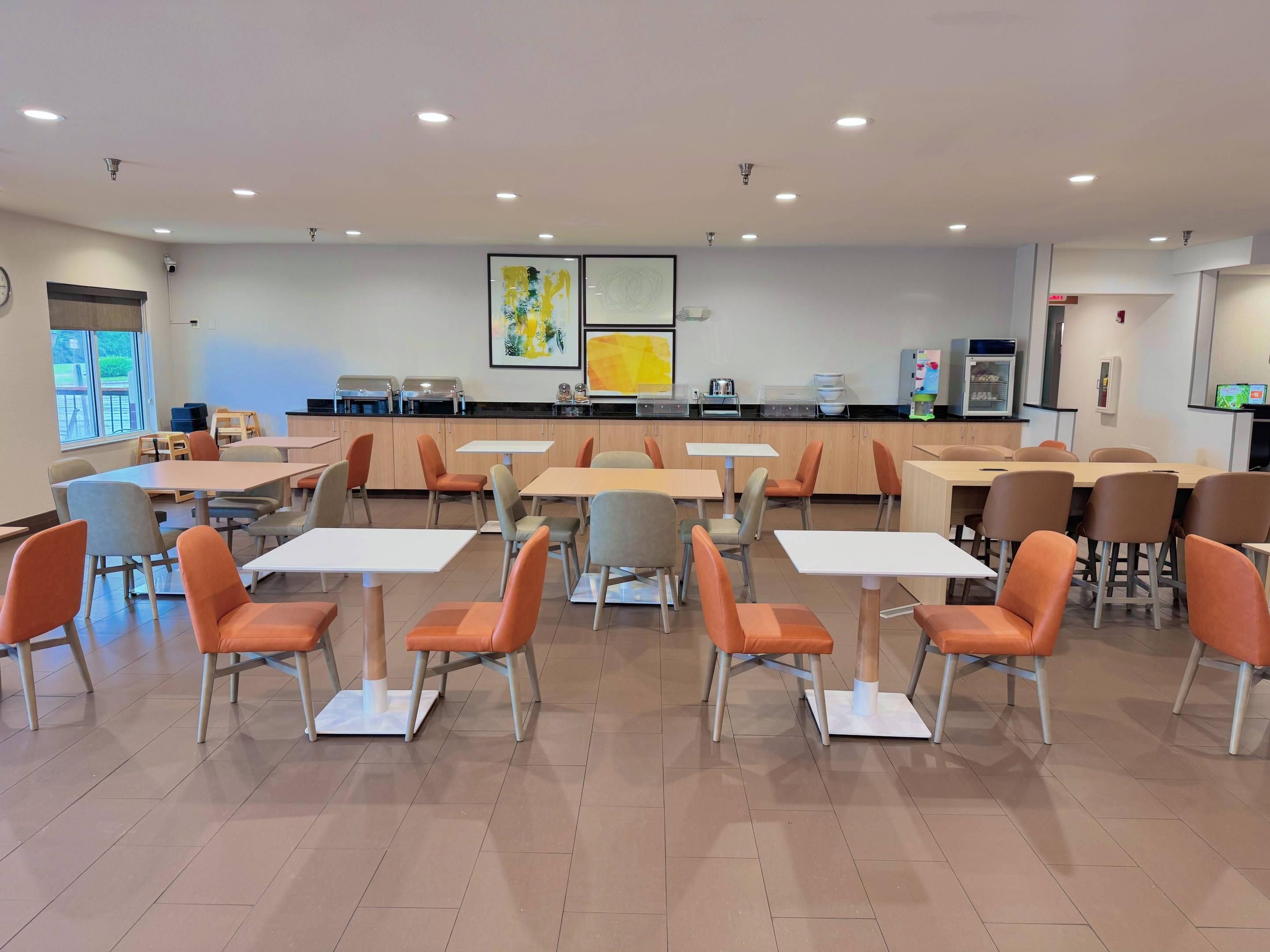 A modern dining area with tables and chairs, a kitchen counter, and artwork on the walls.