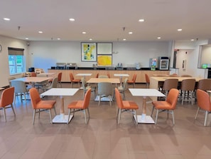 Un espace de repas moderne avec des tables et des chaises, un comptoir de cuisine et des œuvres d’art accrochées aux murs.