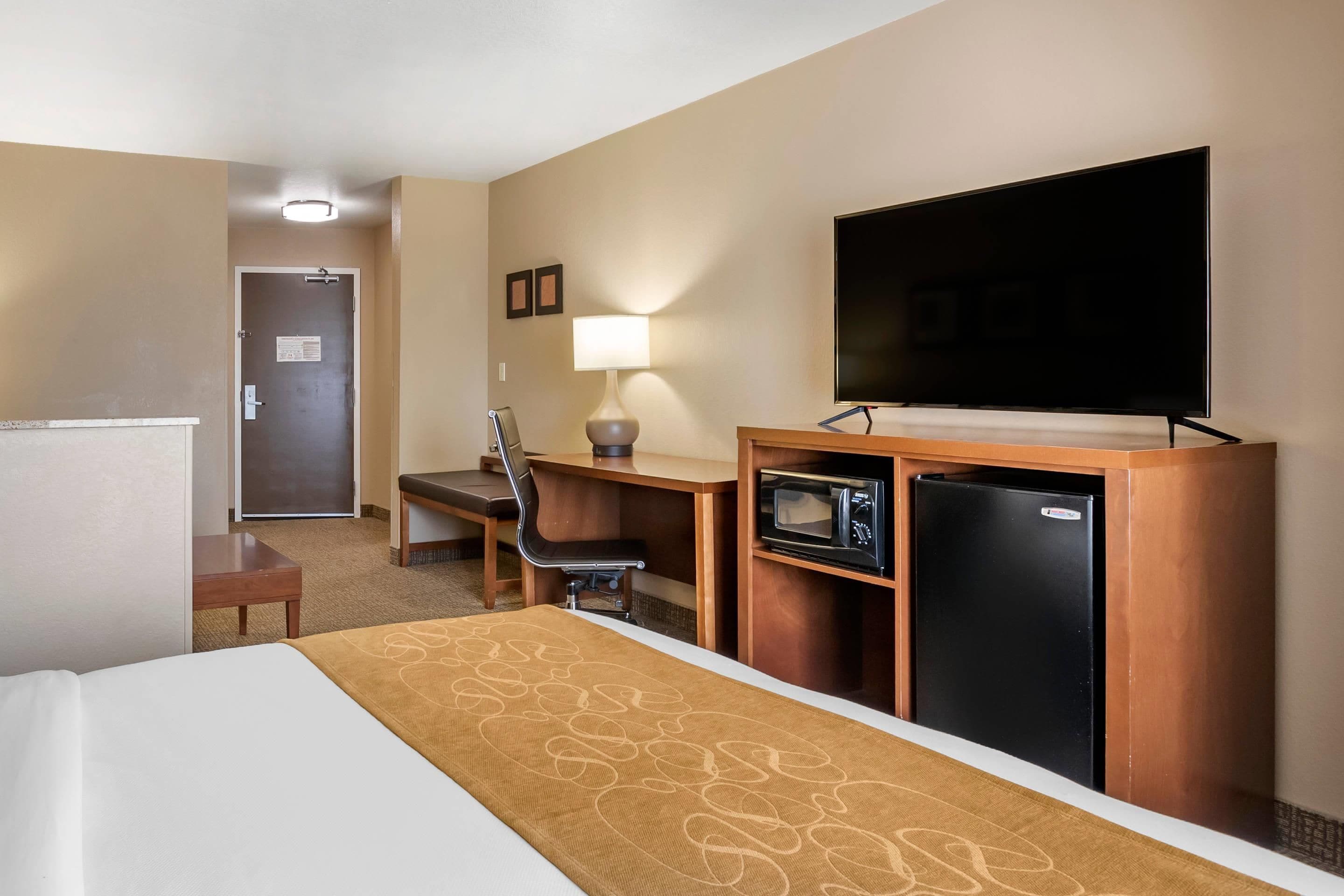 Habitación de hotel con cama, escritorio, silla, televisión, microondas y refrigerador.