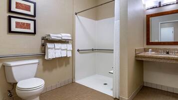A hotel bathroom with a toilet, a shower stall, a towel rack with towels, a sink with a mirror, and two framed pictures on the wall.