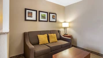 A hotel room with a brown sofa, two yellow cushions, a wooden coffee table, and three framed pictures on the wall.