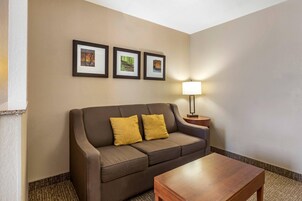 Habitación de hotel con un sofá marrón, dos cojines amarillos, una mesa de centro de madera y tres cuadros en la pared.