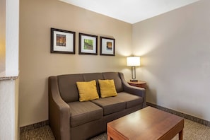 Habitación de hotel con un sofá marrón, dos cojines amarillos, una mesa de centro de madera y tres cuadros en la pared.