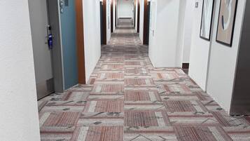 Un pasillo de hotel con alfombra estampada, paredes blancas y varias puertas.