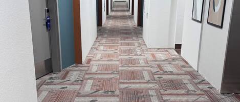 A hotel hallway with patterned carpet, white walls, and multiple doors.