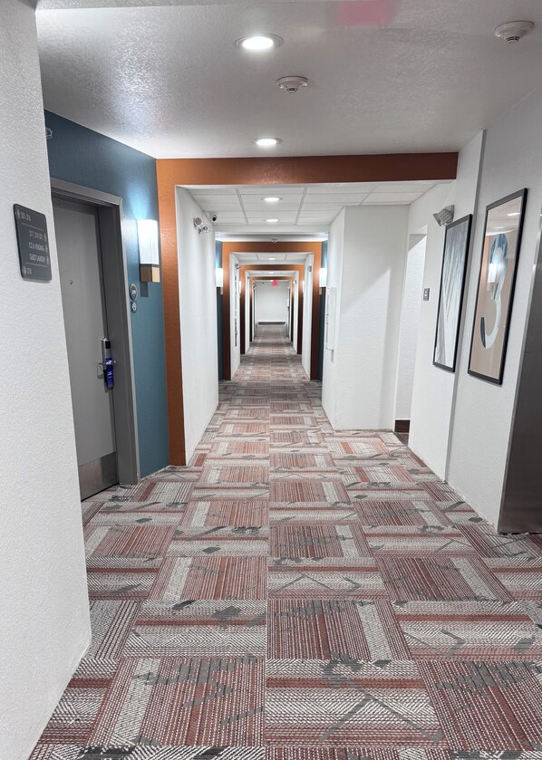 A hotel hallway with patterned carpet, white walls, and multiple doors. - Comfort Suites Coralville I-80 (Coralville)