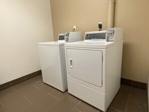 A laundry room with two front-loading washing machines and a commercial dryer. - Comfort Suites Coralville I-80 (Coralville)
