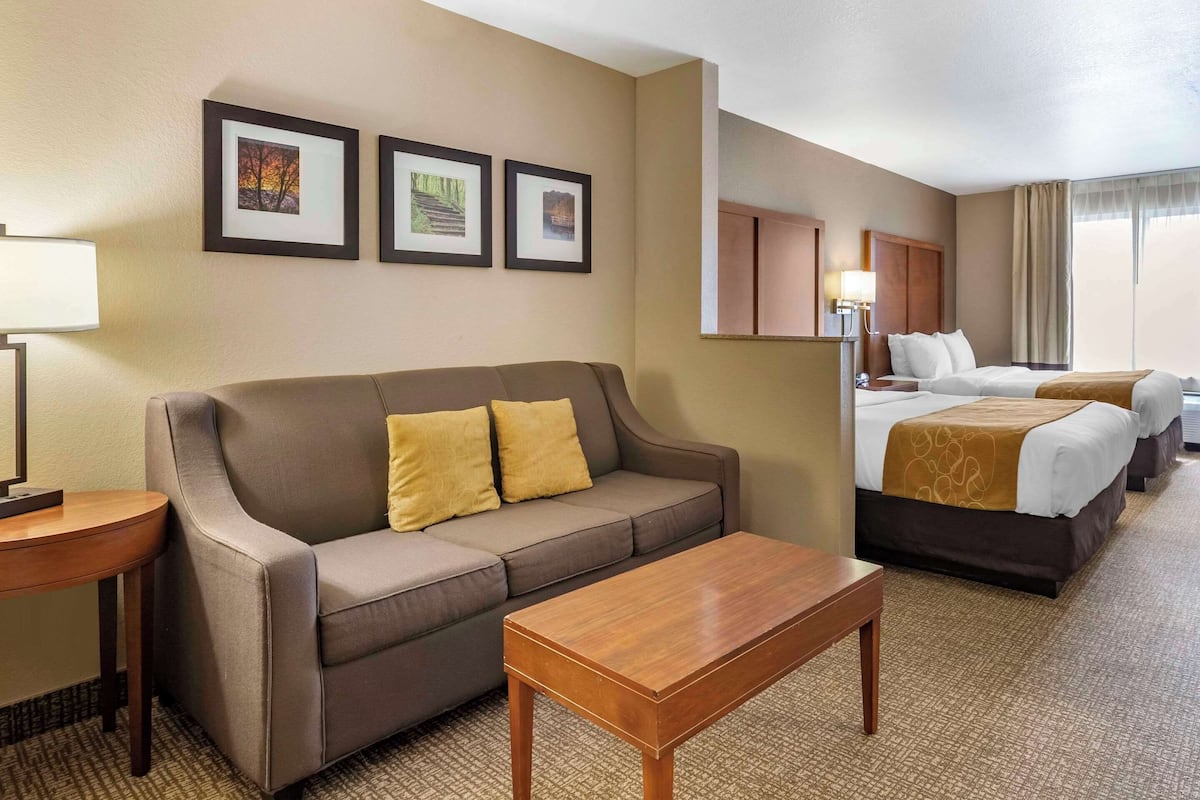 Habitación de hotel con sofá, una mesa de madera, cama con colcha marrón y tres cuadros en la pared.