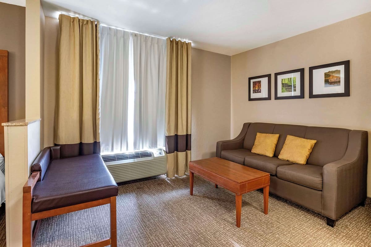 Una habitación de hotel con sofá, una mesita, una ventana con cortinas y tres cuadros en la pared.