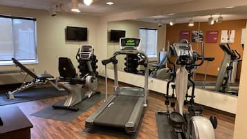 A gym with cardio machines, a mirrored wall, and a wooden floor.