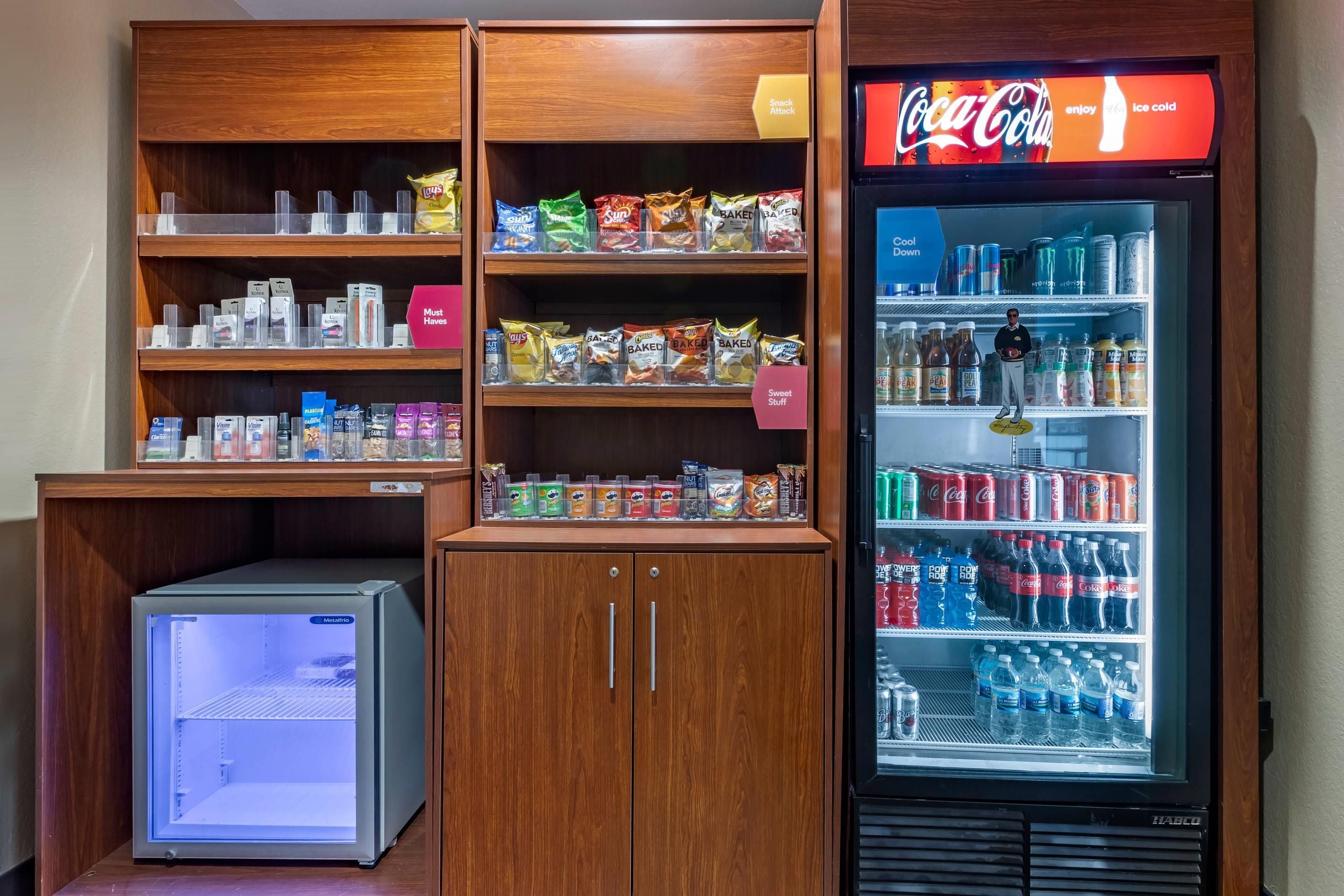 A vending machine stocked with snacks and beverages, a refrigerator with a Coca-Cola sign, and a small cooler with a digital display.