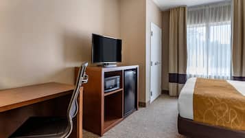 A hotel room with a bed, a desk with a television, a chair, a microwave, and a door.