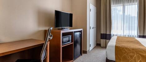 Una habitación de hotel con una cama, un escritorio con televisor, una silla, un microondas y una puerta.