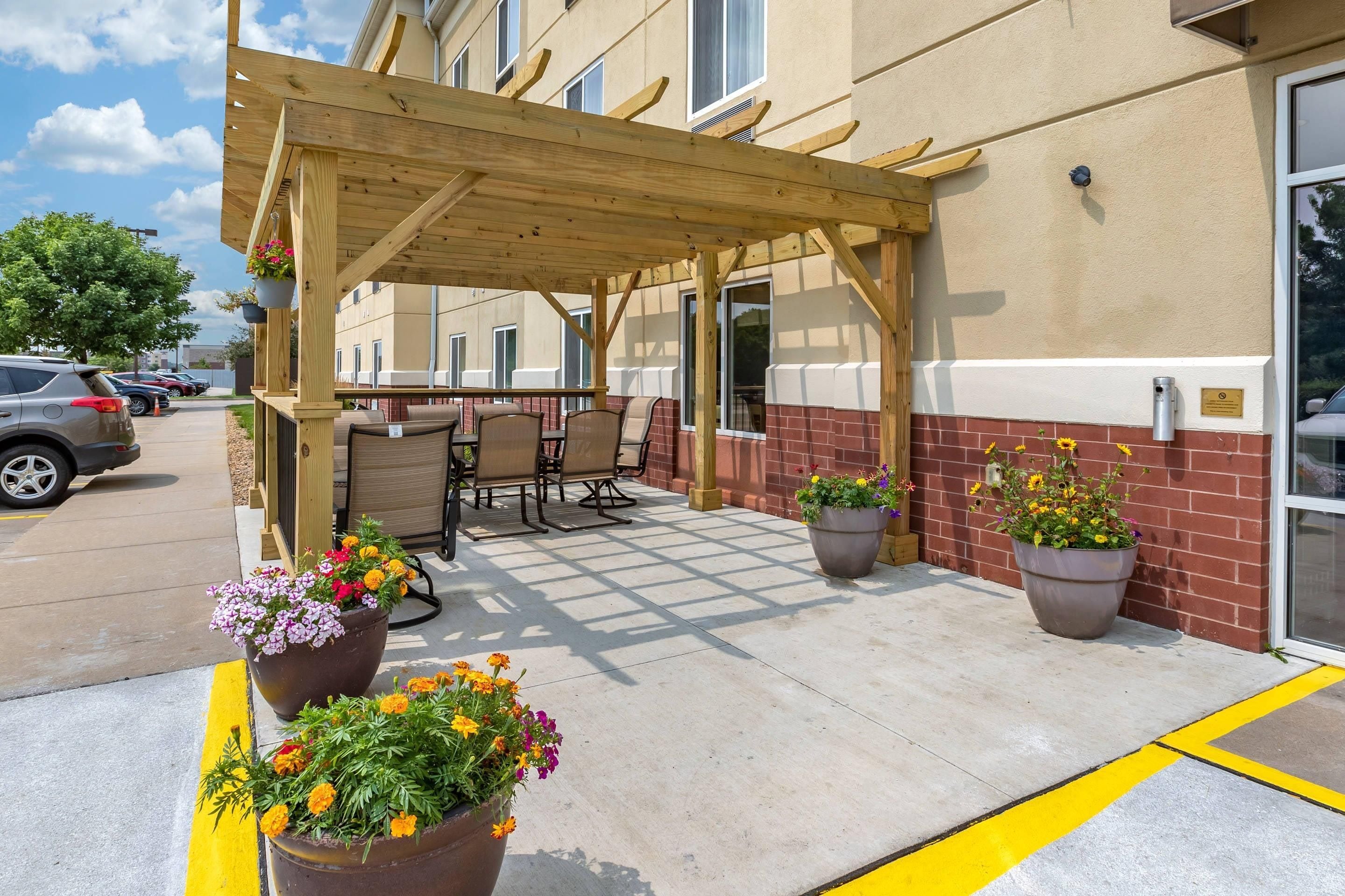 An outdoor patio area with a wooden pergola, seating, and potted plants.