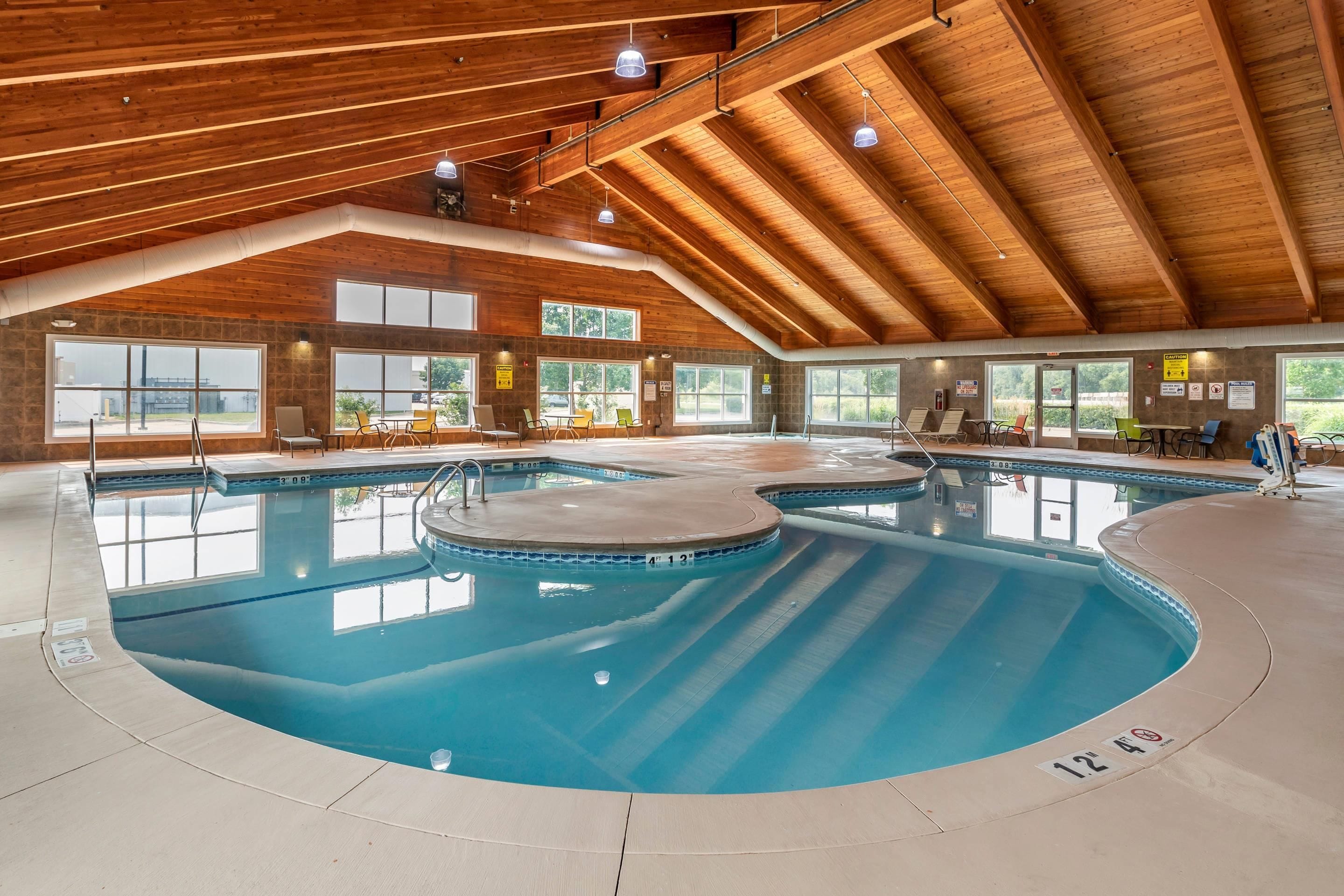 Une piscine intérieure dotée de plusieurs couloirs, de poutres en bois au plafond et de grandes fenêtres.