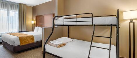 A hotel room with a bunk bed, a separate bed, a lamp, and a window with curtains.