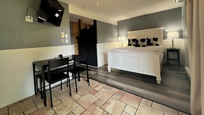 Ein Hotelzimmer mit einem Bett, einem Schreibtisch mit Stühlen, einem Deckenventilator und einem an der Wand befestigten Fernseher.