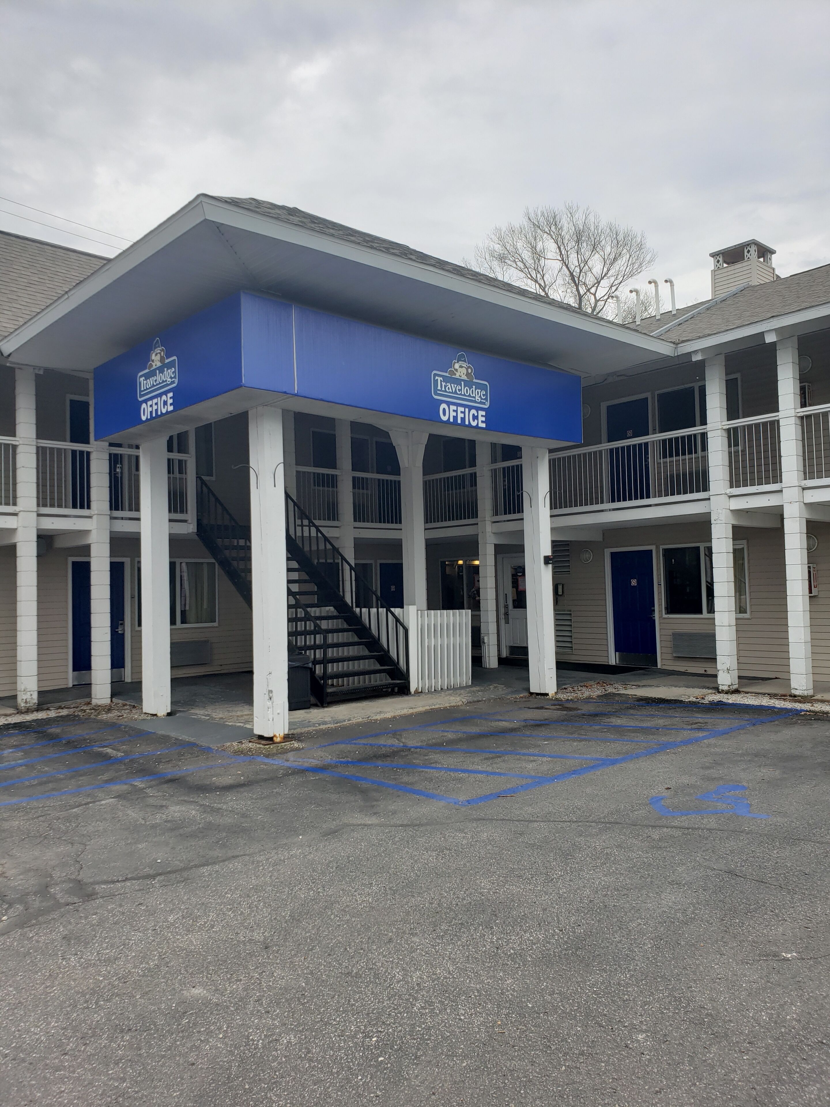 A Travelodge office building with a covered entrance, a staircase, and a parking lot with handicapped spaces.