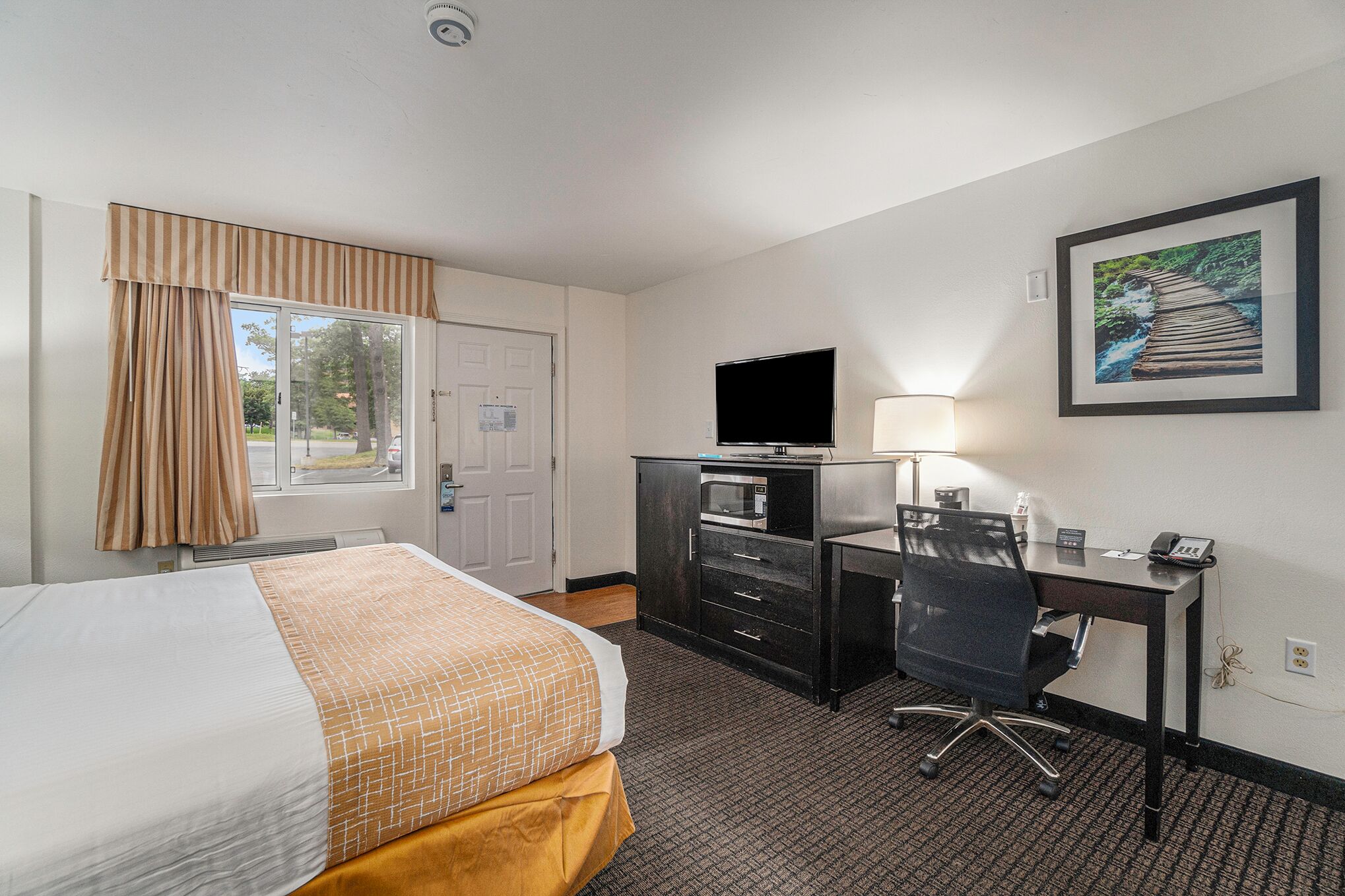 Habitación de hotel con cama, escritorio con computadora, televisor y un cuadro en la pared.